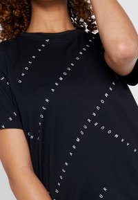 Svart kortärmad t-shirt i bomull med en grafisk design som har texten "UNDER ARMOUR" i vitt, arrangerad diagonalt.