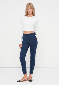 Marine skreddersydde bukser med en glatt tekstur, frontlommer og knappelukking. Kombinert med en hvit cropped langermet topp og slingback-sko.