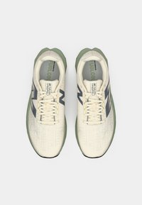 Beige Laufschuhe mit strukturiertem Obermaterial, grüner Sohle und dunkelgrauen Akzenten. Mit Schnürsenkeln und Branding auf der Zunge.