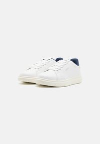 White sneakers with a smooth leather upper, navy accents at the heel, and perforations on the sides for ventilation. Flat rubber sole.