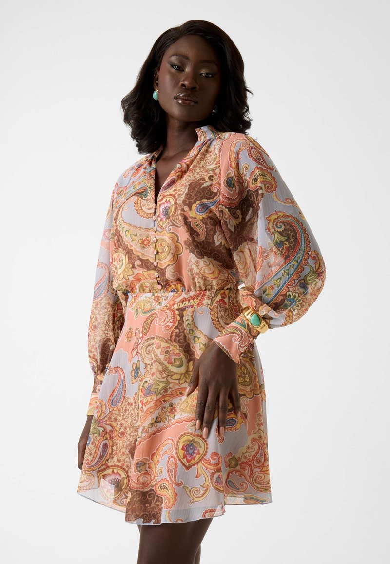 Napitettava mekko, jossa on paisley-kuvio pastellisävyissä, vyötärö kiristettävä ja pitkät hihat. Läpinäkyvää materiaalia, jossa kerätyt hihansuut.