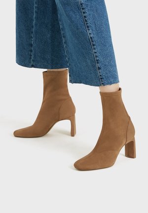 Braune Wildleder-Stiefeletten mit spitzer Zehenpartie und klobigem Absatz. Das Obermaterial zeichnet sich durch eine glatte Textur und eine figurbetonte Silhouette aus.