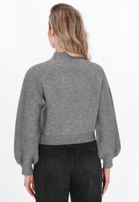 Grå ribbet sweatshirt med høj hals, ballonærmer og cropped kant; parret med mørke jeans, der viser struktur og pasform.