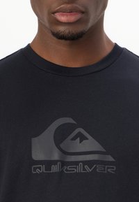 Black cotton t-shirt featuring a large grey Quiksilver logo on the front, with a classic crew neck design and short sleeves.