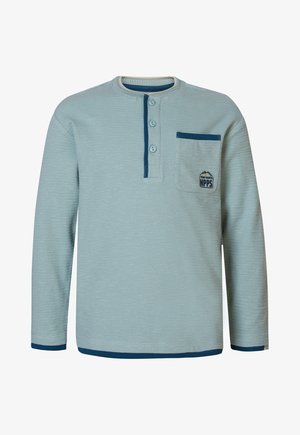 Jasnoniebieska bluzka z długim rękawem o teksturowej powierzchni, z trzema guzikami przy szyi oraz kieszonką na piersi z grafiką logo. Marynarskie akcenty.