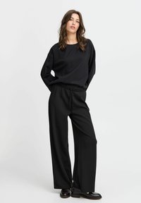 Schwarzes, locker sitzendes Sweatshirt mit langen Ärmeln, kombiniert mit hoch taillierten, schwarzen, weiten Hosen, die einen elastischen Bund und ein minimales Design aufweisen.