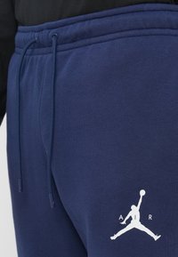 Jūras spēku sporta bikses, kas izgatavotas no mīksta auduma ar elastīgu jostas vietu, ar balto Jumpman logo uz kreisā kājas. Iekļauta auklas detaļa.