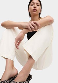 Crème-kleurige wijde broek met een gladde textuur. Gecombineerd met een zwart geribbelde top en gemusterde sandalen.