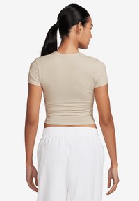 Beige színű cropped póló rövid ujjal és testhezálló fazonnal. Simaság jellemzi, a hátrészen ráncolt részletekkel, fehér nadrággal párosítva.