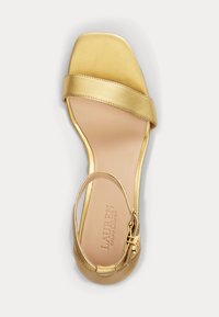 Zlaté saténové sandály na podpatku s hranatou špičkou, širokým páskem přes nohu a nastavitelným nártem s kovovými doplňky.