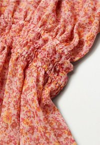 Tissu floral rose avec texture plissée, présentant des nuances d'orange et de jaune dans un matériau léger et aérien. Détails de surface doux et froissés.