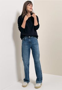 Sudadera negra con capucha y mangas largas combinada con vaqueros acampanados de color azul claro. Los accesorios incluyen zapatos blancos con acentos azules.