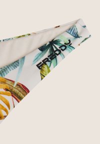 Bikini-alusosa, jolla on trooppinen lehtikuvio vihreinä ja keltaisina valkoisella taustalla, sileä ja joustava kangas sekä musta brändilogo.