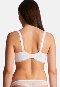 Soutien-gorge en dentelle blanche avec des bretelles ajustables, une fermeture arrière à crochet et à œil, et des motifs floraux avec des bords festonnés.