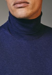 Maglione a collo alto blu navy, texture morbida, design aderente, presenta un alto colletto e un tessuto a maglia liscia. Nessun motivo o accento visibile.