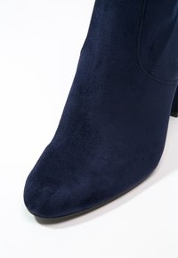 Bottine en daim bleu marine avec un bout pointu et un petit talon large. Texture lisse et design minimaliste, sans éléments métalliques ni accents visibles.