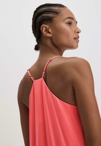 Välja ärmlös klänning i ljus korall med justerbara remmar, mjukt tyg och avslappnad passform, som framhäver ryggdesignen.