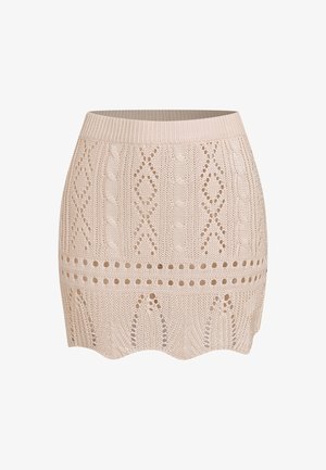 Mini-jupe beige tricotée avec motifs en losanges et torsades, rangées d'œillets, large ceinture et ourlet festonné.