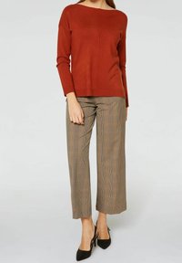 Pull en tricot couleur rouille avec un col large et des manches longues, associé à un pantalon court à carreaux marron et des talons noirs pointus.