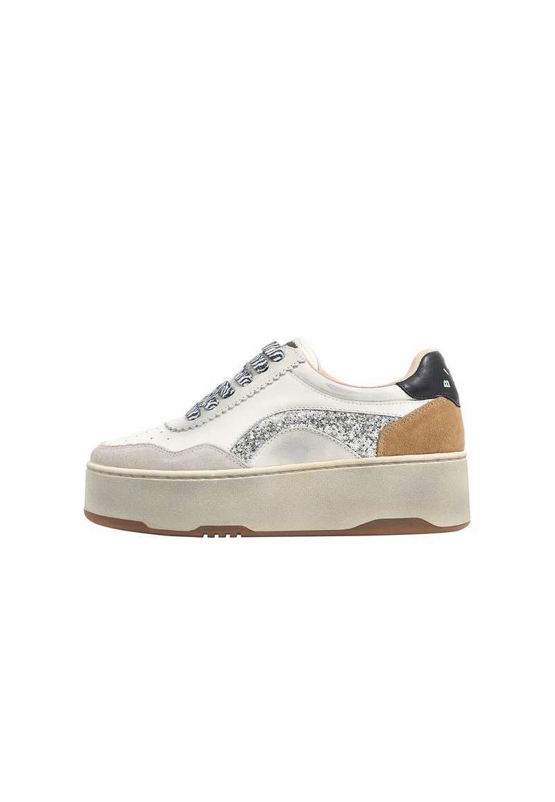 Zapatillas de plataforma con parte superior de cuero blanco y gris, detalles de purpurina plateada y un parche de ante marrón. Presentan una suela de goma gruesa y una lengüeta negra en el talón.