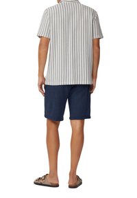 Korte mouwen overhemd met een kraag en verticale blauwe strepen op lichte stof, gecombineerd met marineblauwe shorts en bruine sandalen.