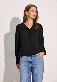 Blusa nera a maniche lunghe con scollatura a V e dettaglio dei bottoni, abbinata a jeans azzurri chiari a vestibilità ampia. Tessuto morbido e vestibilità rilassata.