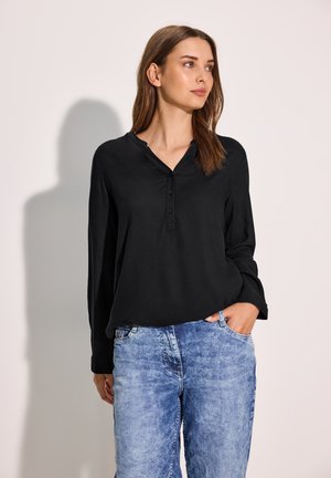 Blouse noire à manches longues avec un décolleté en V et des détails de boutons, associée à un jean bleu clair, légèrement ajusté. Tissu doux et coupe décontractée.
