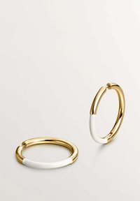 Aros de oro con un acento de esmalte blanco, forma circular y un acabado brillante. Incluye un detalle de cierre seguro.