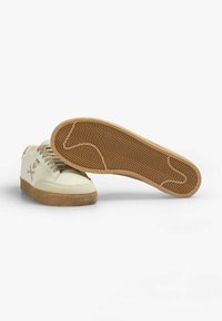 Beige Sneaker aus strukturiertem Leder, mit Gummisohle und Schnürdesign. Auffälliges Fischgrätprofil auf der braunen Außensohle.