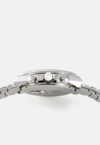 Orologio in acciaio inossidabile argentato con una lunetta texturizzata, due pulsanti e un bracciale in metallo spazzolato. Presenta una cassa circolare con dettagli incisi.