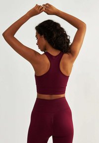 Bordowy zestaw odzieży sportowej z sportowym stanikiem typu racerback o strukturalnym wzorze oraz legginsami z wysokim stanem. Gładki, elastyczny materiał.