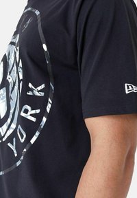 T-shirt en coton noir avec un grand graphique camouflage réfléchissant portant le texte "NEW YORK" et le logo sur le devant, à manches courtes.