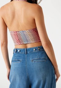 Hæklede halterneck crop top i flerfarvet bølgemønster, parret med højtaljede blå denimbukser med baglommer og knaplukning.