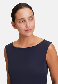 Haut sans manches bleu marine avec un col rond, texture lisse et design minimaliste. Présente une poche discrète sur le côté gauche.