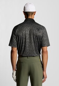 Kortärmad polotröja i svart med ett geometriskt mönster, med en kontrasterande krage och logodetalj på axeln. Kombineras med olivgröna byxor.