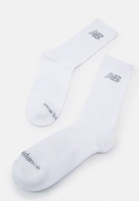 Calcetines de deporte blancos hechos de tela suave, con un logo gris de "New Balance" en la parte superior y el texto "balance" en la suela.