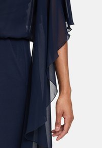 Navyblaues Kleid mit fließenden, durchsichtigen Ärmeln. Der Stoff ist leicht und strukturiert, mit sanften Rüschen an den Rändern.