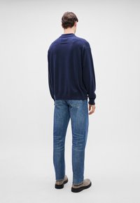 Ναυτικό πλεκτό πουλόβερ με μακριά μανίκια, διαθέτει μικρή τσέπη στην πλάτη. Συνδυασμένο με ανοιχτό μπλε τζιν κανονικής γραμμής και γκρι παπούτσια.