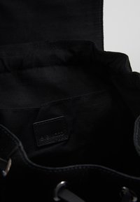 Interiér černé textilní tašky s malou vnitřní kapsou, na které je přišitá cedulka, a stříbrnými očky u otevření tašky.