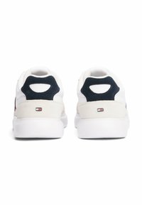 Sneaker bianco con tomaia in pelle liscia, dettagli in suede blu navy sul tallone e interno in tessuto. Presenta un ritaglio circolare sul tab del tallone.