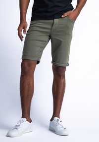 Oliivinvihreät shortsit käännetyillä hihoilla, valmistettu puuvillasta, slim fit -malliset ja etutaskut. Yhdistetty valkoisiin tennareihin.