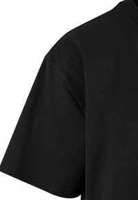 Black cotton t-shirt with a round neckline and short sleeves; smooth texture and clean edges. Close-up view of the shoulder and sleeve.