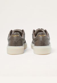 Brązowe skórzane trampki z teksturowanym tyłem i jasnokolorową gumową podeszwą. Złote logo na pięcie. Miękka wyściółka widoczna przy otwarciu.