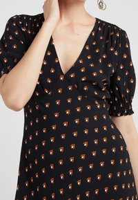 Vestido negro con un profundo escote en V, mangas abullonadas y puños elásticos. Presenta un patrón floral repetido en naranja y blanco en toda la tela.