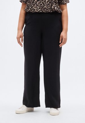 Pantaloni neri a gamba larga realizzati in tessuto leggero, con vestibilità comoda e vita elasticizzata. Abbinati a sneakers bianche.