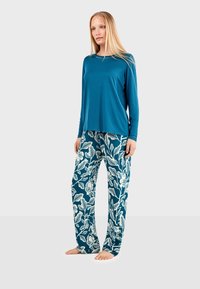 Haut à manches longues en teal associé à un pantalon ample avec un motif floral blanc sur fond teal foncé. Tissu doux et léger.