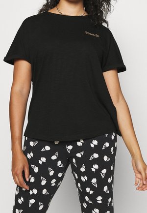 Kvinde iført en sort T-shirt med "favorite" broderet på brystet og sorte bukser med hvidt blomsterprint.