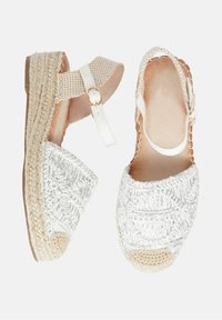 Sandali espadrilles bianchi con tomaia in tessuto intrecciato, cinturino alla caviglia con fibbia dorata e suola a zeppa coperta di juta, con texture intricata.