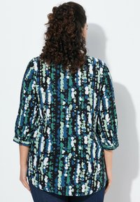 Blusa stampata con maniche a 3/4; presenta motivi astratti blu, verdi e bianchi su uno sfondo nero; tessuto morbido e orlo arrotondato.