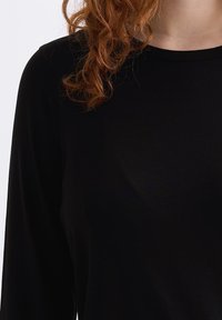 Schwarzes Langarmshirt aus glattem Stoff, mit rundem Ausschnitt und lockerer Passform. Sichtbare Textur und Fall hervorgehoben.